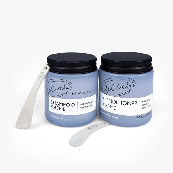 UpCircle Haircare Duo set featuring two minimalist glass bottles on a travertine plinth with free cosmetic spatulas.