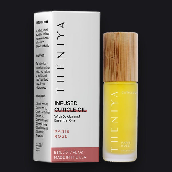 Theniya Paris Rose Infused Cuticle Oil in a clear glass dropper bottle with dried rose petals, resting on a travertine slab.