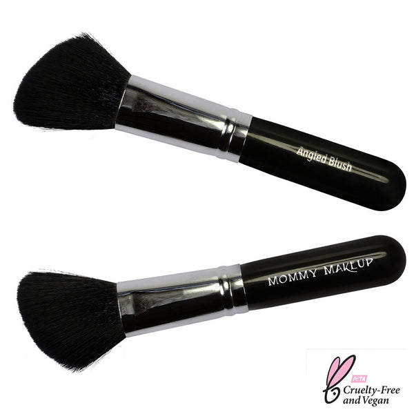 Mommy Makeup angled blush brush featuring soft synthetic bristles and a sleek handle resting on a textured travertine base.