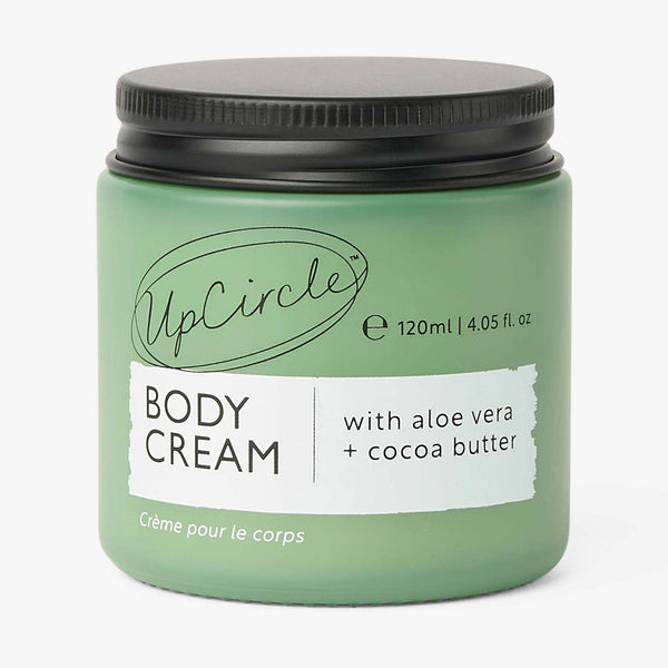 UpCircle Natural Body Cream in a chic, minimalist glass jar sitting atop a textured travertine stone plinth.