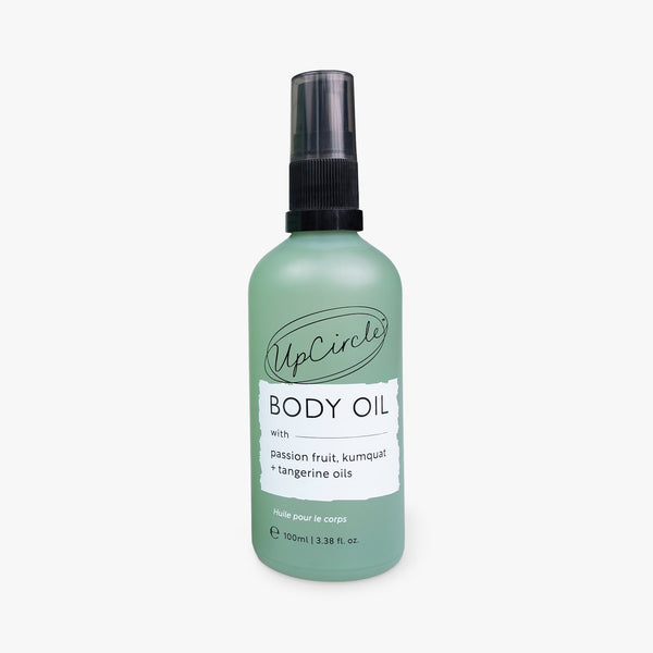 UpCircle Body Oil with Passion Fruit Oil in a sleek amber glass bottle resting on a textured travertine surface.