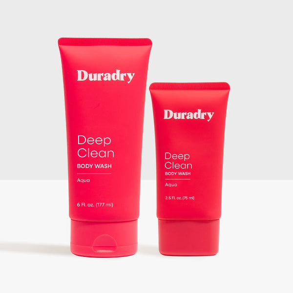 Duradry Body Wash Duo bottles resting on a textured travertine plinth against a backdrop of raw champagne silk.