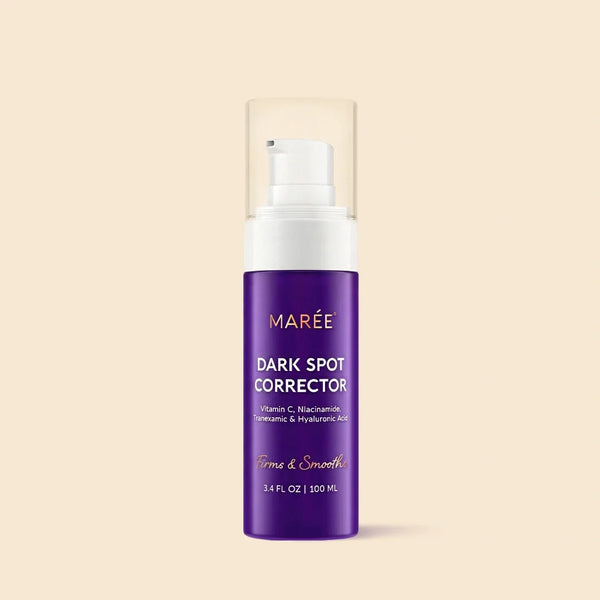 Marée Face & Body Serum for Dark Spots in a minimalist glass bottle resting on a beige travertine surface.