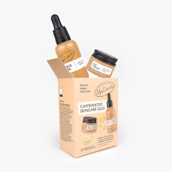 UpCircle The Caffeinated Duo eye cream and face scrub set displayed in amber glass jars on a textured beige surface.