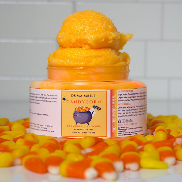 Adorn Collective Candy Corn Foaming Sugar Scrub in a premium glass jar, resting on a textured travertine plinth.