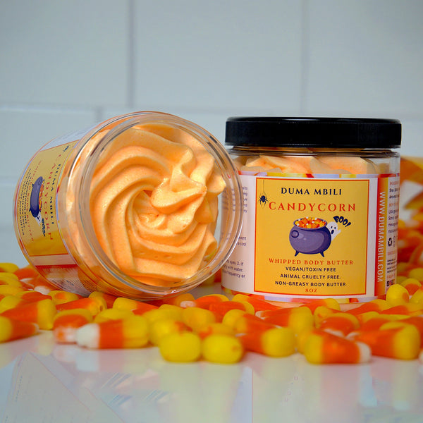 Adorn Collective Candy Corn Whipped Body Butter in a minimalist glass jar set on raw silk against a travertine plinth.