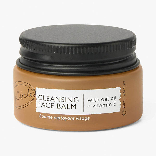 UpCircle travel-size cleansing face balm in a sleek glass jar, resting on a beige stone surface with soft morning light.