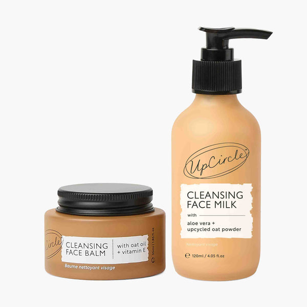UpCircle Double Cleansing Duo set featuring glass bottles on a beige travertine surface with soft natural morning light.