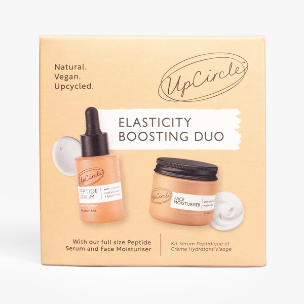 UpCircle Elasticity Boosting Duo featuring glass serum and cream bottles resting on a textured cream-colored surface.