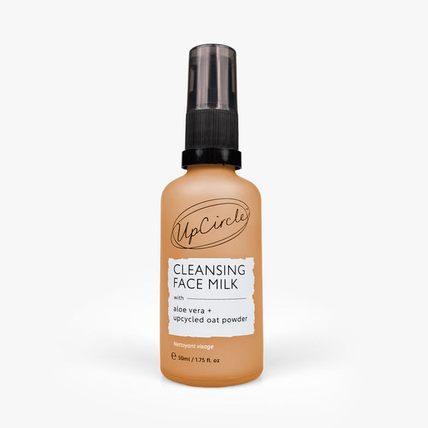 UpCircle Cleansing Face Milk with Oat Powder in a compact, travel-sized glass bottle set against a textured stone surface.