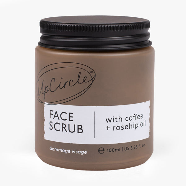 UpCircle Face Scrub in a glass jar resting on a textured travertine surface, highlighting natural coffee and oil grains.