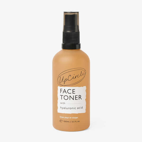 UpCircle Face Toner with Hyaluronic Acid in a sustainable glass bottle, displayed on a textured travertine surface.