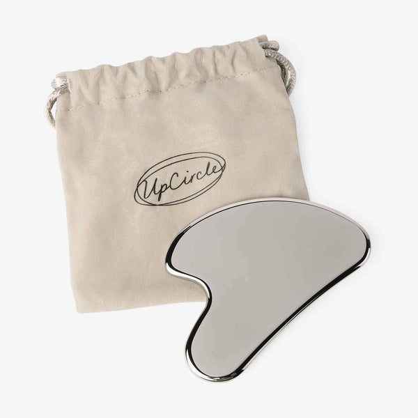UpCircle Gua Sha facial massage stone crafted from smooth, rose-toned stone, resting on a textured linen surface.