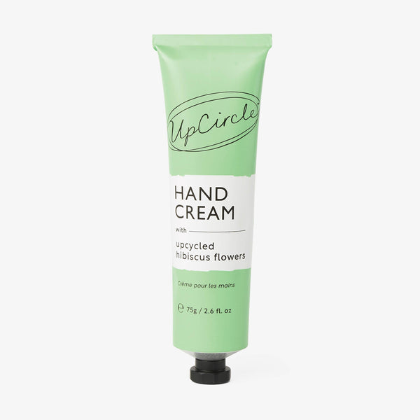 UpCircle Hand Cream with Hibiscus Flowers in a sleek minimalist tube resting on a textured travertine plinth.