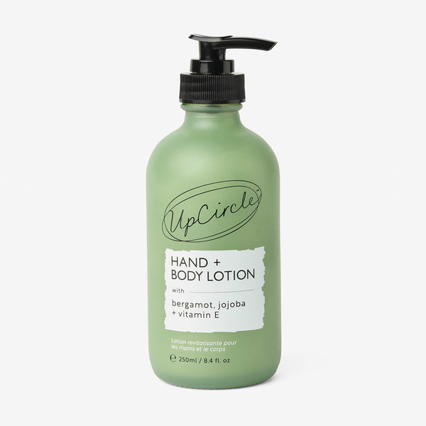 UpCircle Hand + Body Lotion in a minimalist glass bottle resting on a travertine plinth with soft morning light.