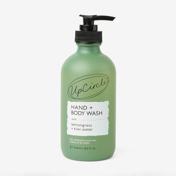 UpCircle Natural Hand + Body Wash in a minimalist amber glass bottle sitting on a textured travertine surface.