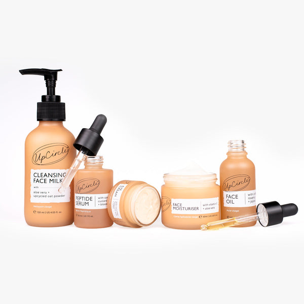 UpCircle 5-Step Essentials Bundle featuring sustainably packaged skincare bottles on a textured travertine plinth.