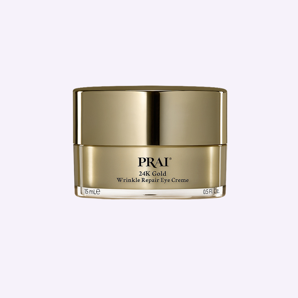 PRAI Beauty 24K Gold Wrinkle Repair Eye Creme jar resting on a textured travertine surface.