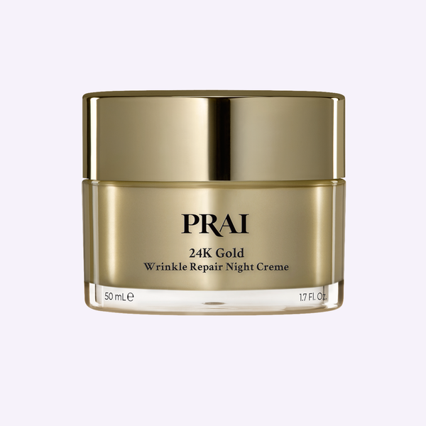 PRAI Beauty 24K Gold Wrinkle Repair Night Creme in a reflective gold-trimmed glass jar resting on a neutral stone surface.