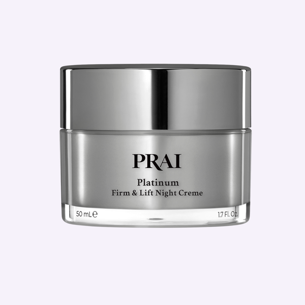 PRAI Beauty Platinum Firm & Lift Night Creme in a sleek silver-toned luxury jar resting on an organic travertine stone.