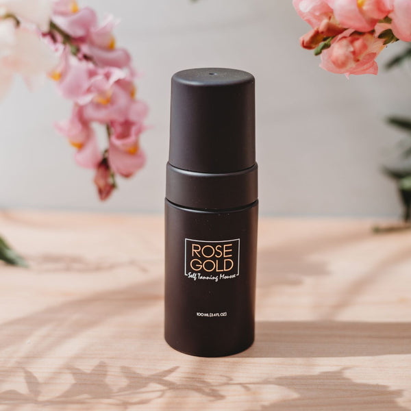 Rose Gold Sunless travel size self tanning mousse bottle resting on a minimalist travertine stone surface.