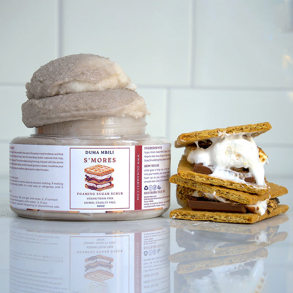 Adorn Collective S’mores Foaming Sugar Scrub in a glass jar, set against a warm travertine backdrop.