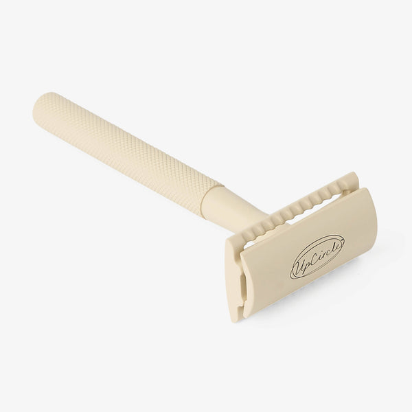 UpCircle plastic-free safety razor resting on a textured travertine plinth against a backdrop of soft oatmeal raw silk.