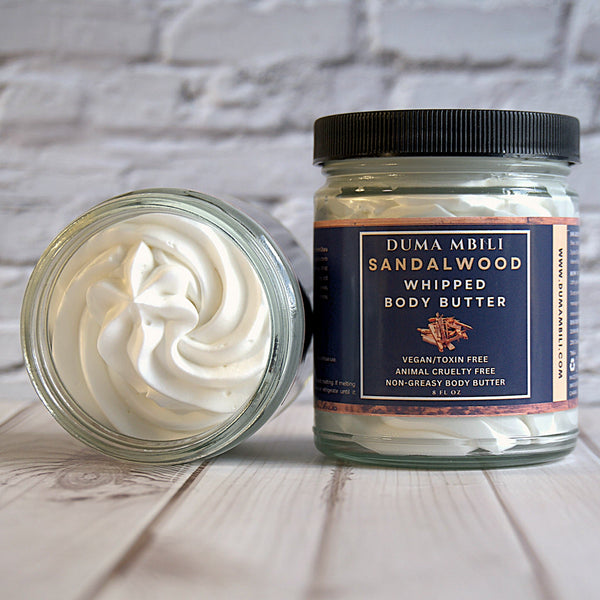 Adorn Collective Sandalwood Whipped Body Butter in an elegant frosted glass jar resting on a textured travertine plinth.