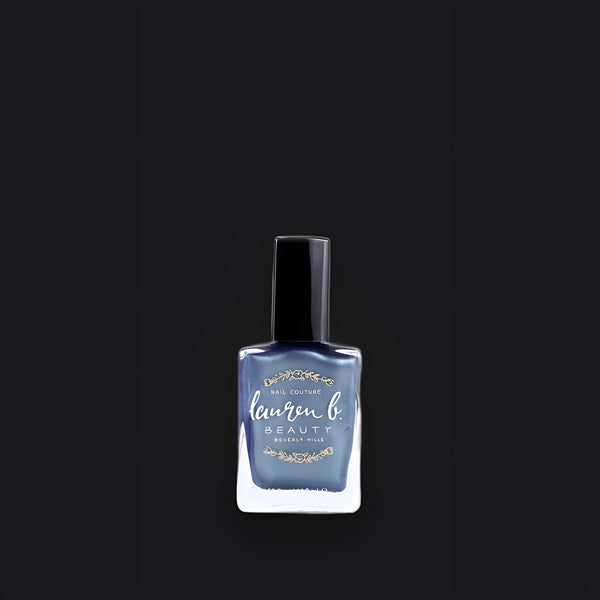 Lauren B. Beauty Downtown Skyline nail polish in a sleek glass bottle with a gold cap, set against a travertine plinth.