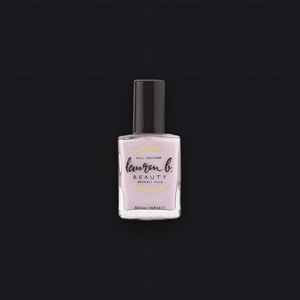 Lauren B. Beauty Pale Sand Paradise nail polish bottle resting on a travertine plinth, featuring a sleek, minimalist cap.