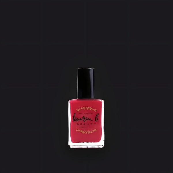 Lauren B. Beauty Polo Lounge Punch nail polish bottle displayed on a beige travertine plinth with elegant glass curves.