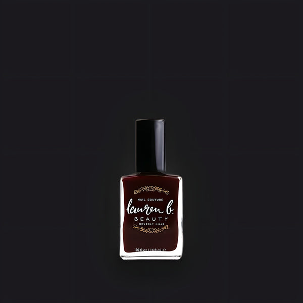 Lauren B. Beauty The Chateau nail polish bottle in a sleek glass container, showcased on a textured beige surface.